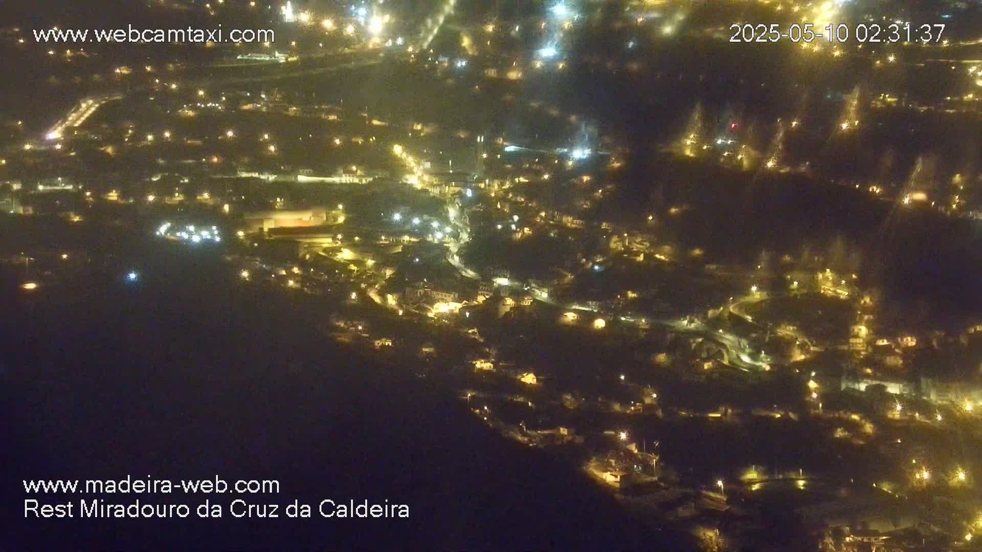 A nighttime, aerial view shows a hillside town illuminated by many small lights.