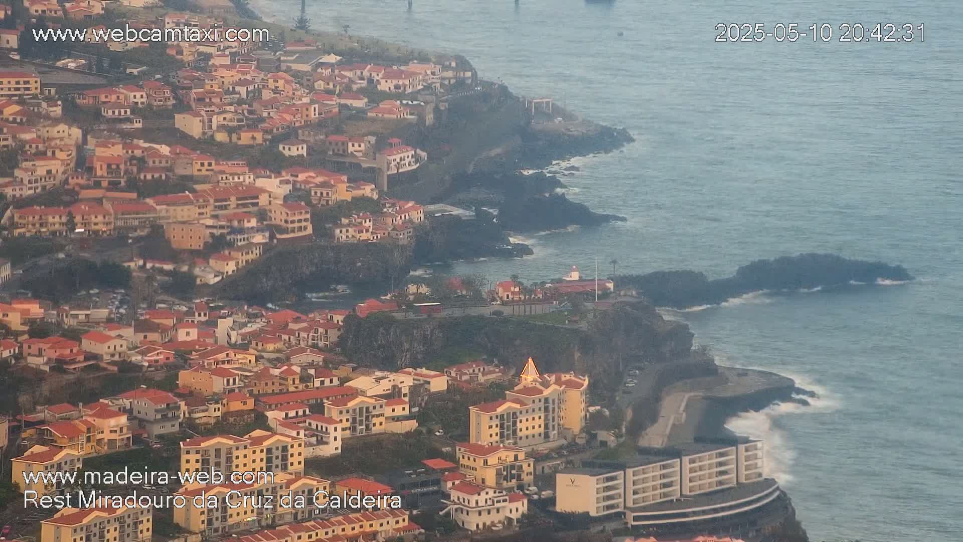 A coastal town with many low-rise buildings, situated on a cliff overlooking a sea with small waves under an overcast sky.