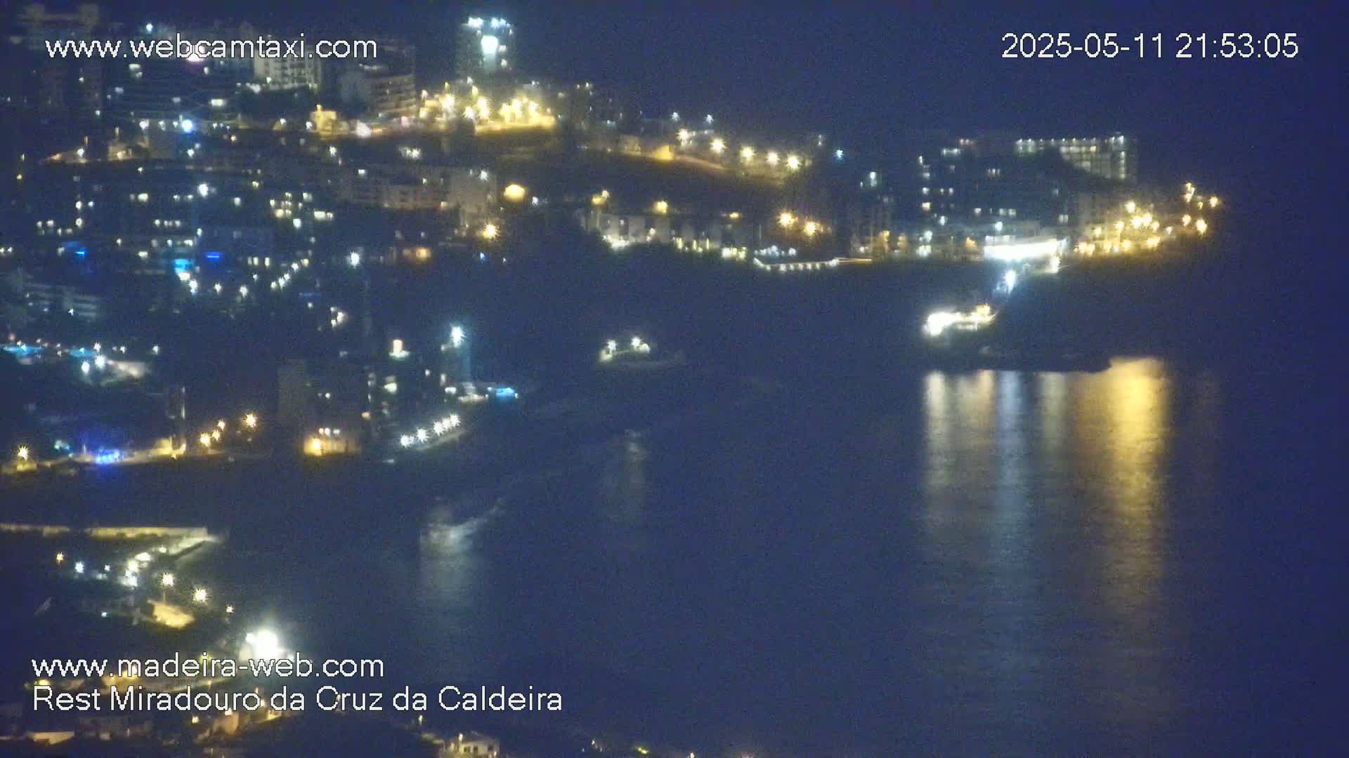 A nighttime view of a coastal town with its lights reflected on dark water.