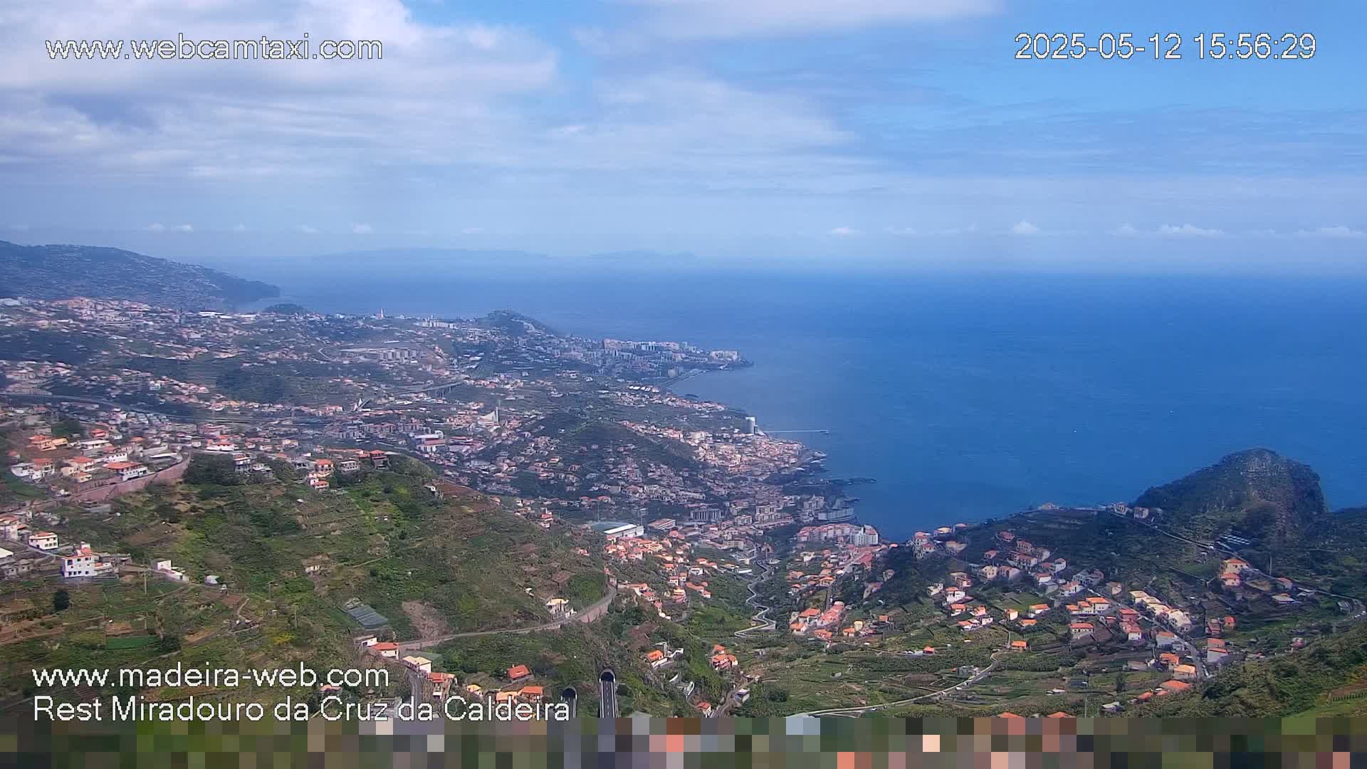 A coastal town nestled on a hillside overlooking a calm ocean under a mostly clear sky.