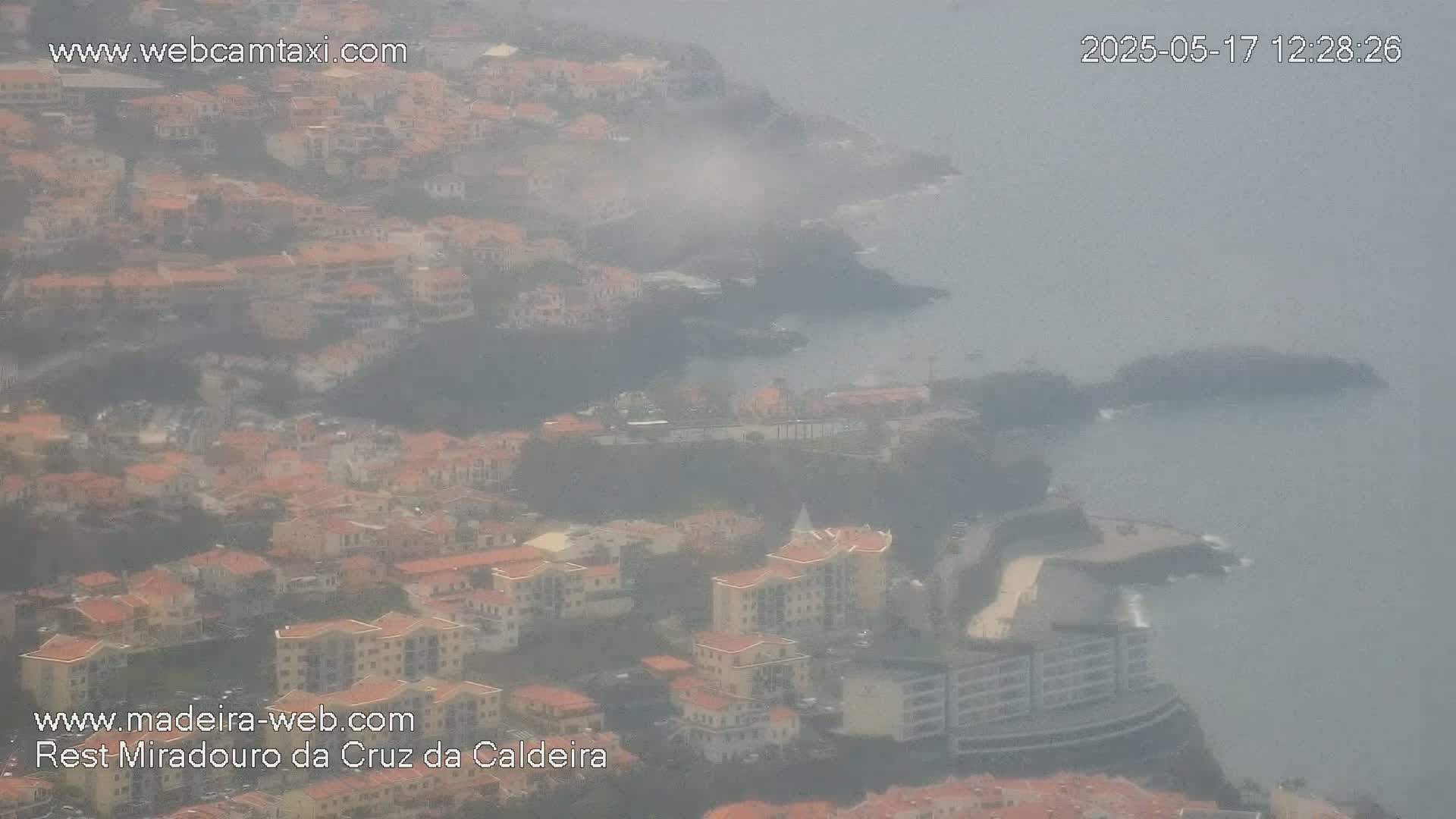 A hazy coastal town with many low-rise buildings, some taller structures, and a rocky shoreline is visible in the distance.