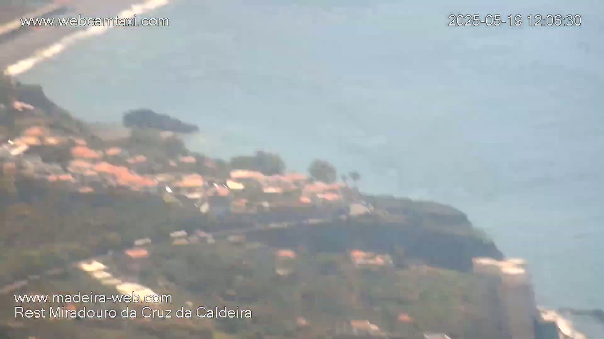A hazy, long-range view shows a coastal town nestled on a hillside overlooking a calm ocean.