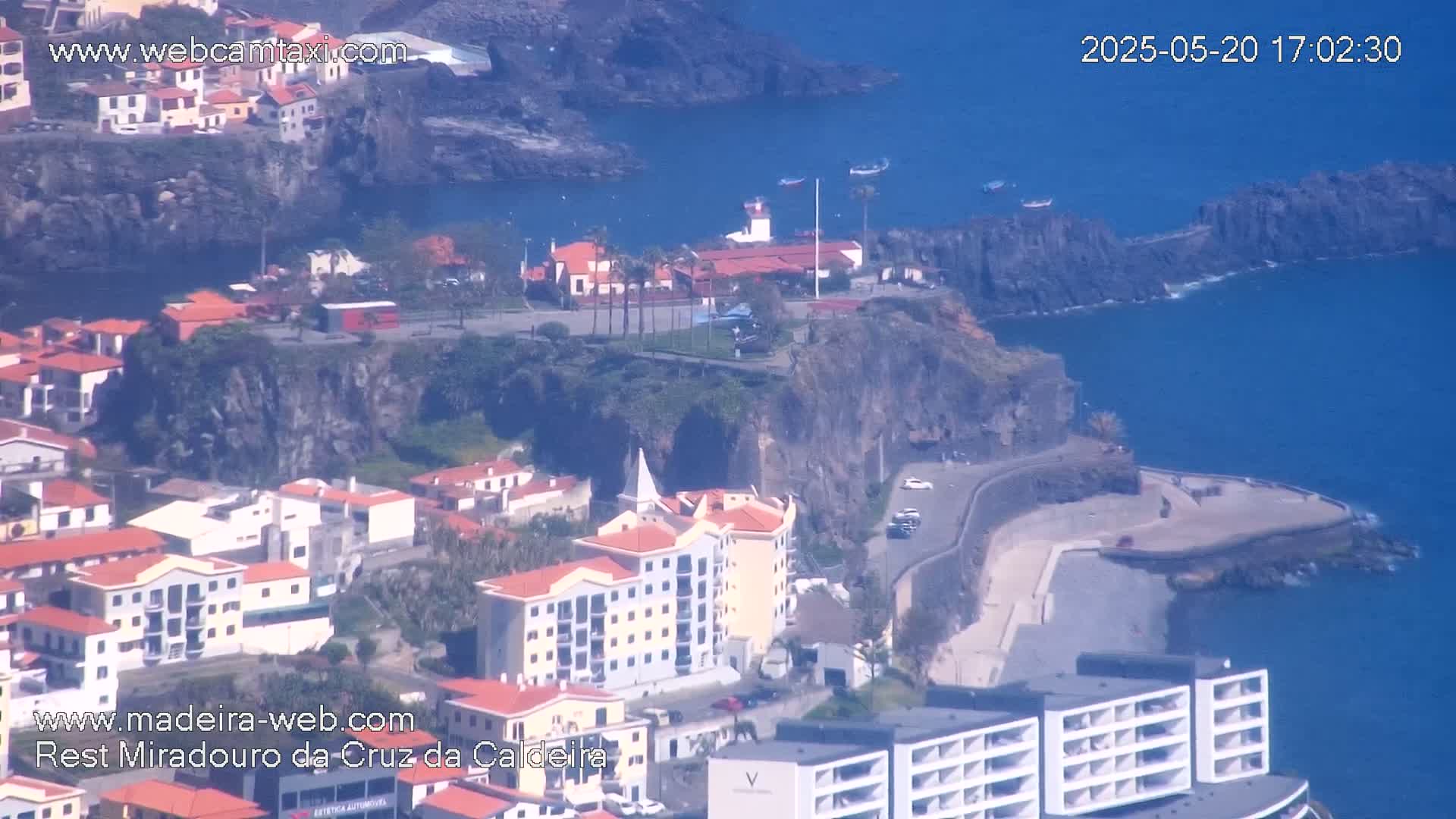 A coastal town nestled on a cliffside overlooking a calm blue ocean on a sunny day.