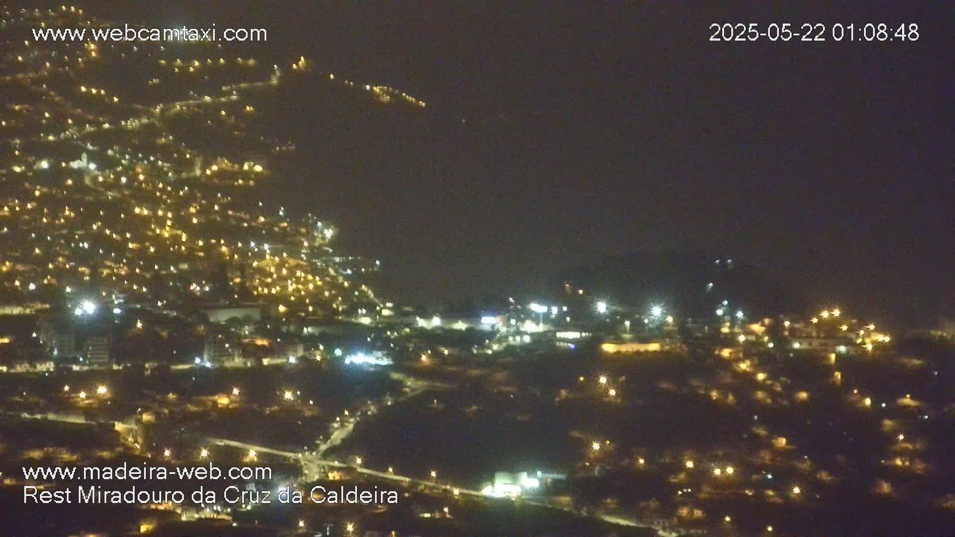 A nighttime aerial view shows a hillside town illuminated by numerous lights under a dark, clear sky.