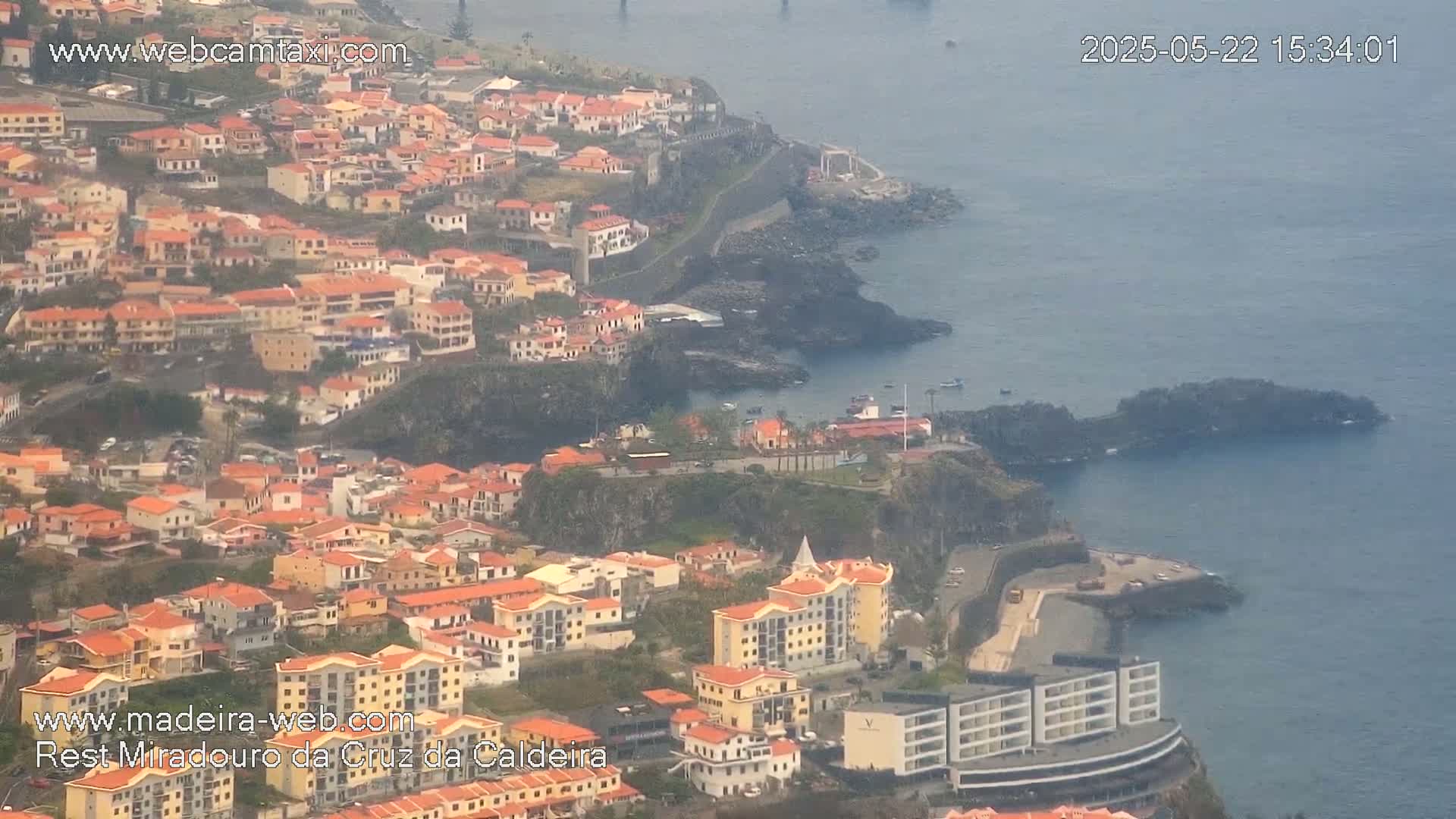 A coastal town with many low-rise buildings clings to a cliffside overlooking a calm ocean on an overcast day.