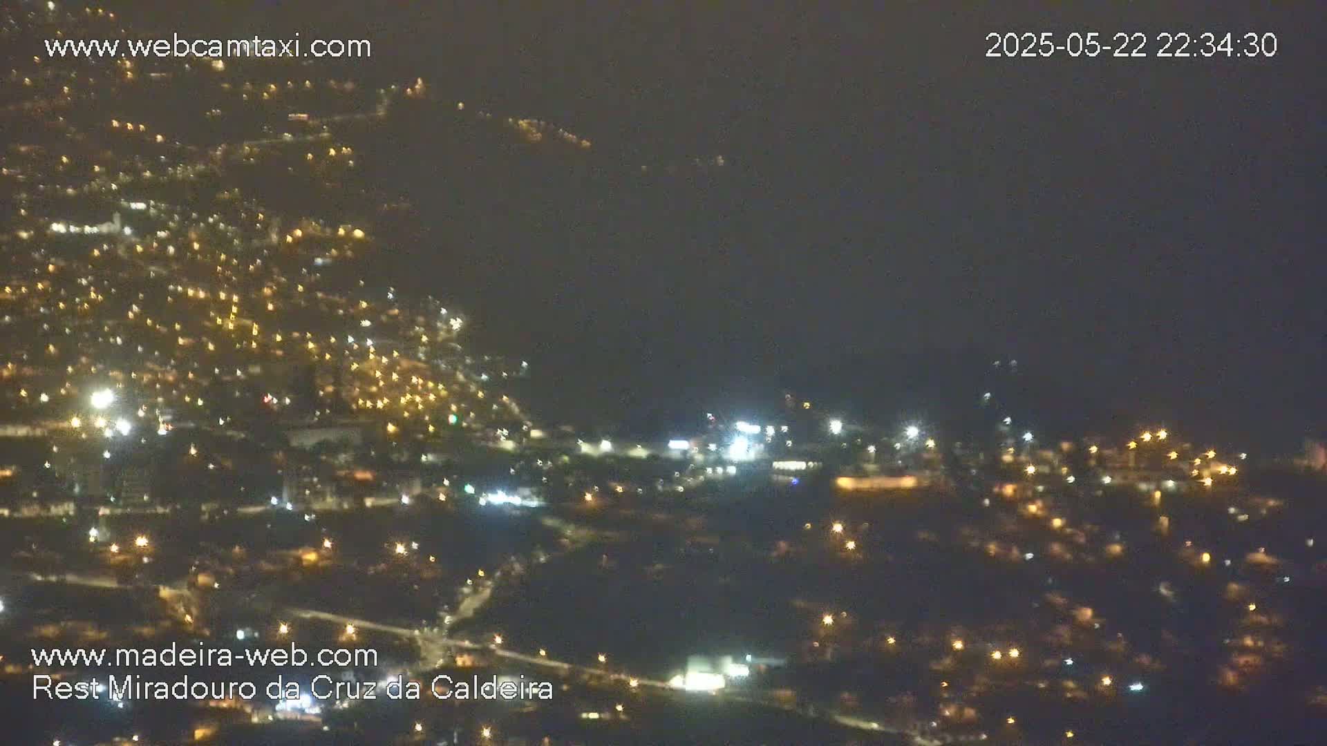 A nighttime, slightly hazy view of a city spread across a hillside, illuminated by numerous small lights.