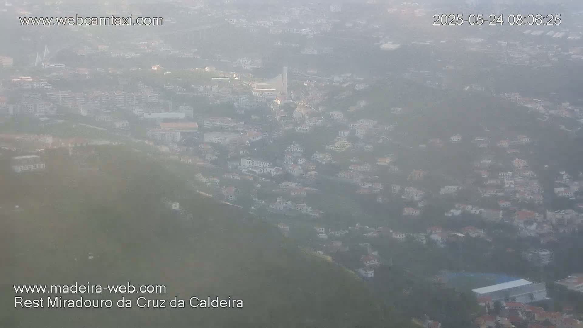 A hazy view of a town nestled in a hillside, possibly shrouded in morning mist or fog.