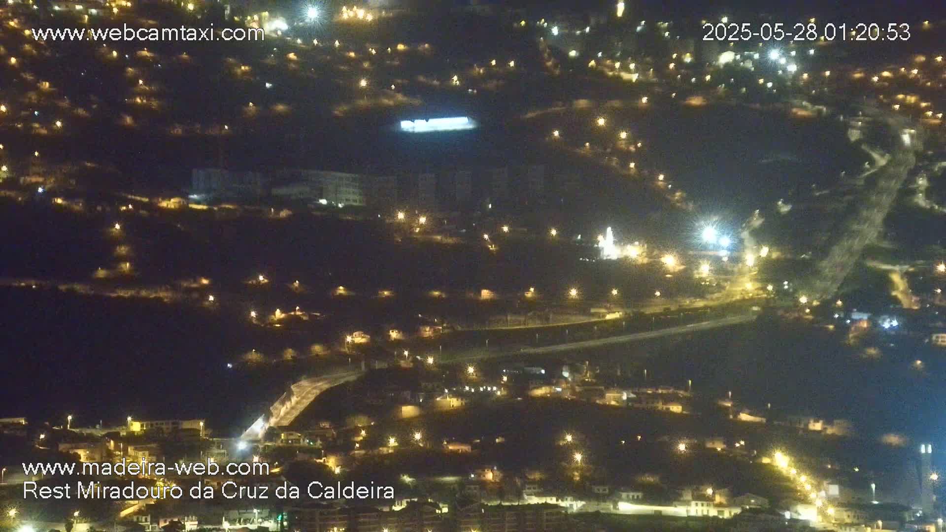 A nighttime aerial view of a town illuminated by streetlights, spread across a hillside.