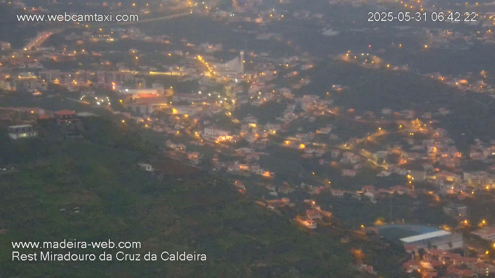A hillside town at twilight is dimly lit, with hazy atmospheric conditions.