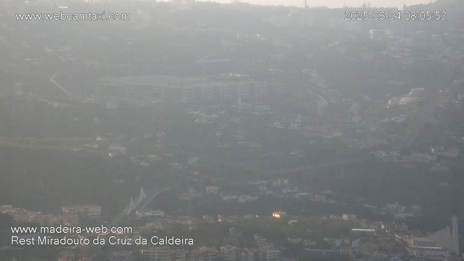 A hazy, long-distance view of a city nestled in a valley, possibly at sunrise or sunset.
