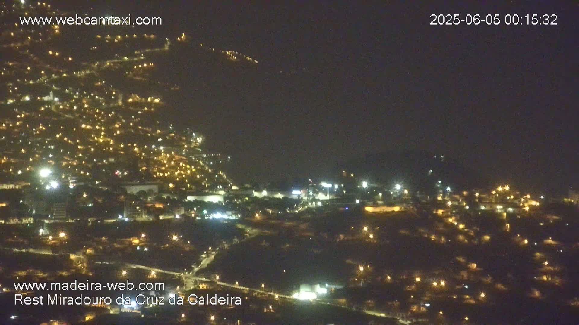 A nighttime, aerial view of a hillside town illuminated by many scattered lights under a dark, hazy sky.