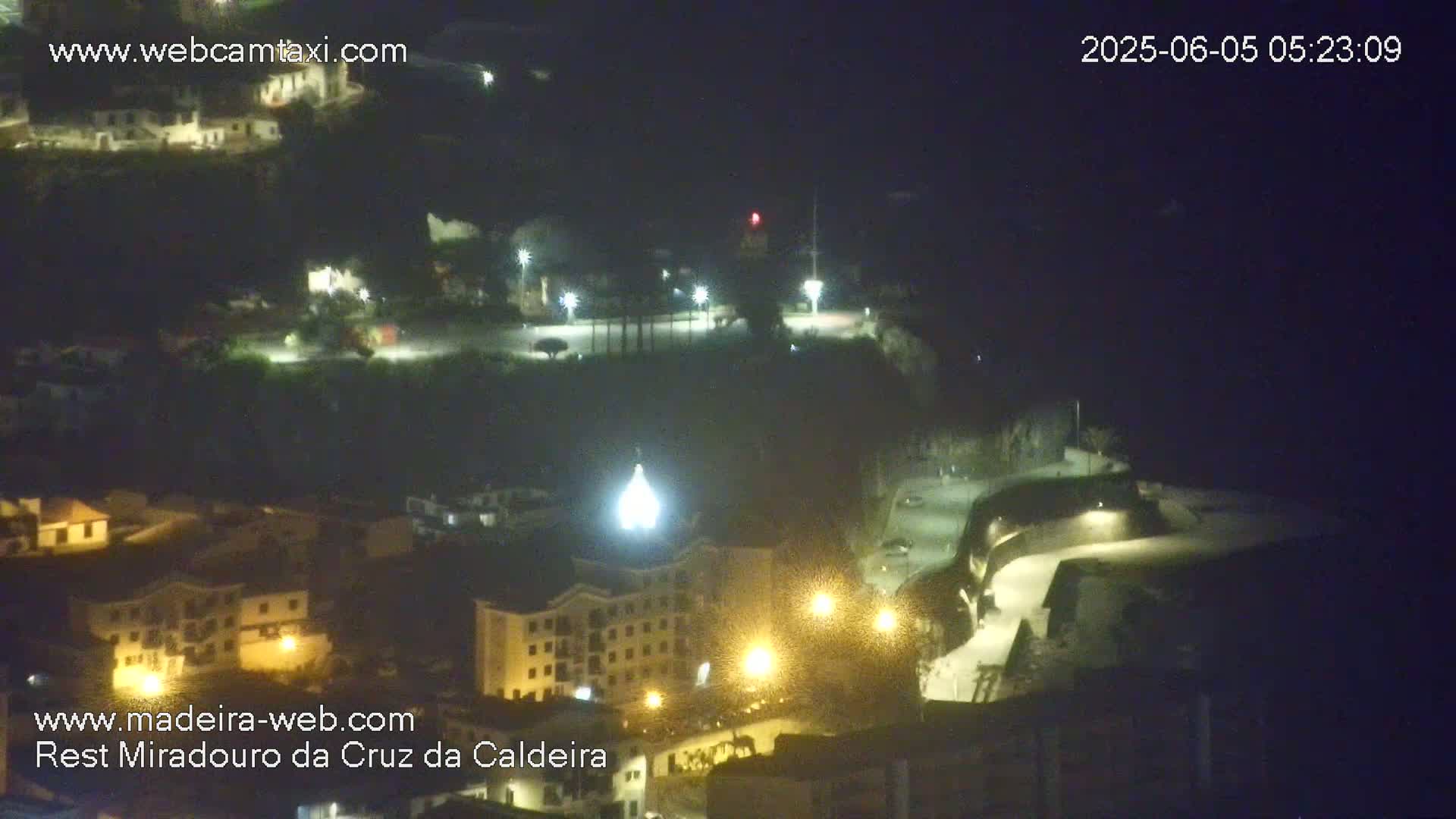 A nighttime, high-angle view of a town nestled on a hillside, illuminated by streetlights.