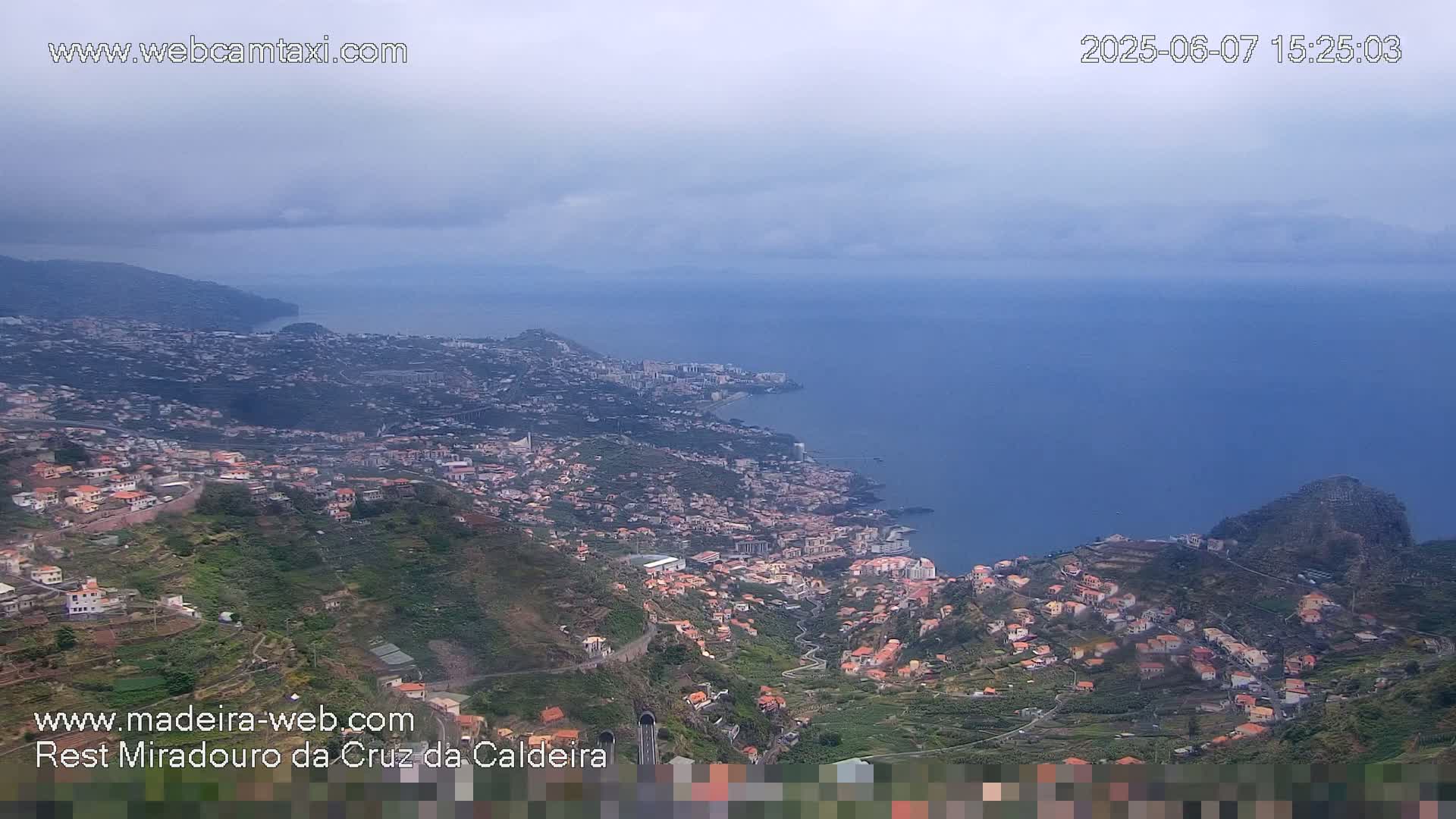 A coastal town nestled into a hillside overlooks a calm ocean under a cloudy sky.