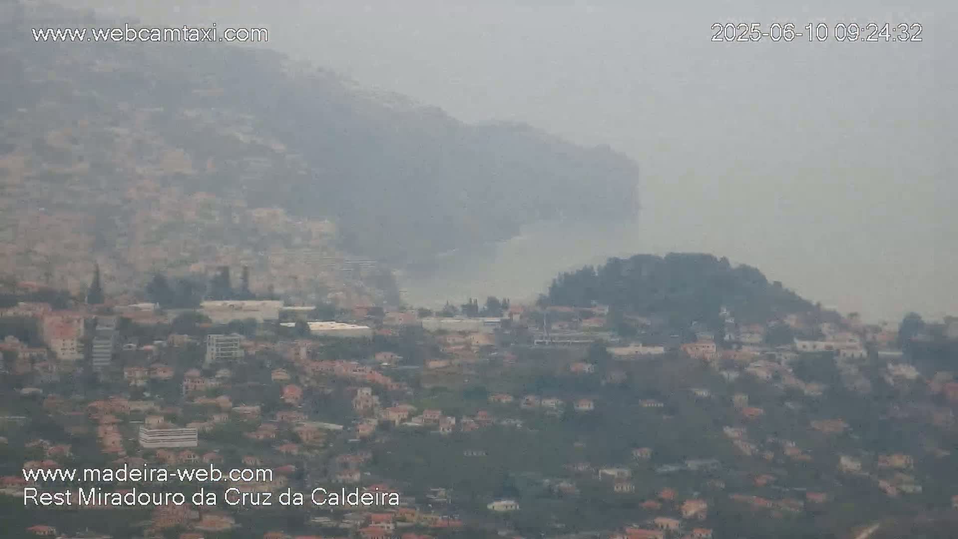 A hazy, distant view shows a coastal town nestled between hills, with the ocean visible in the mid-ground.