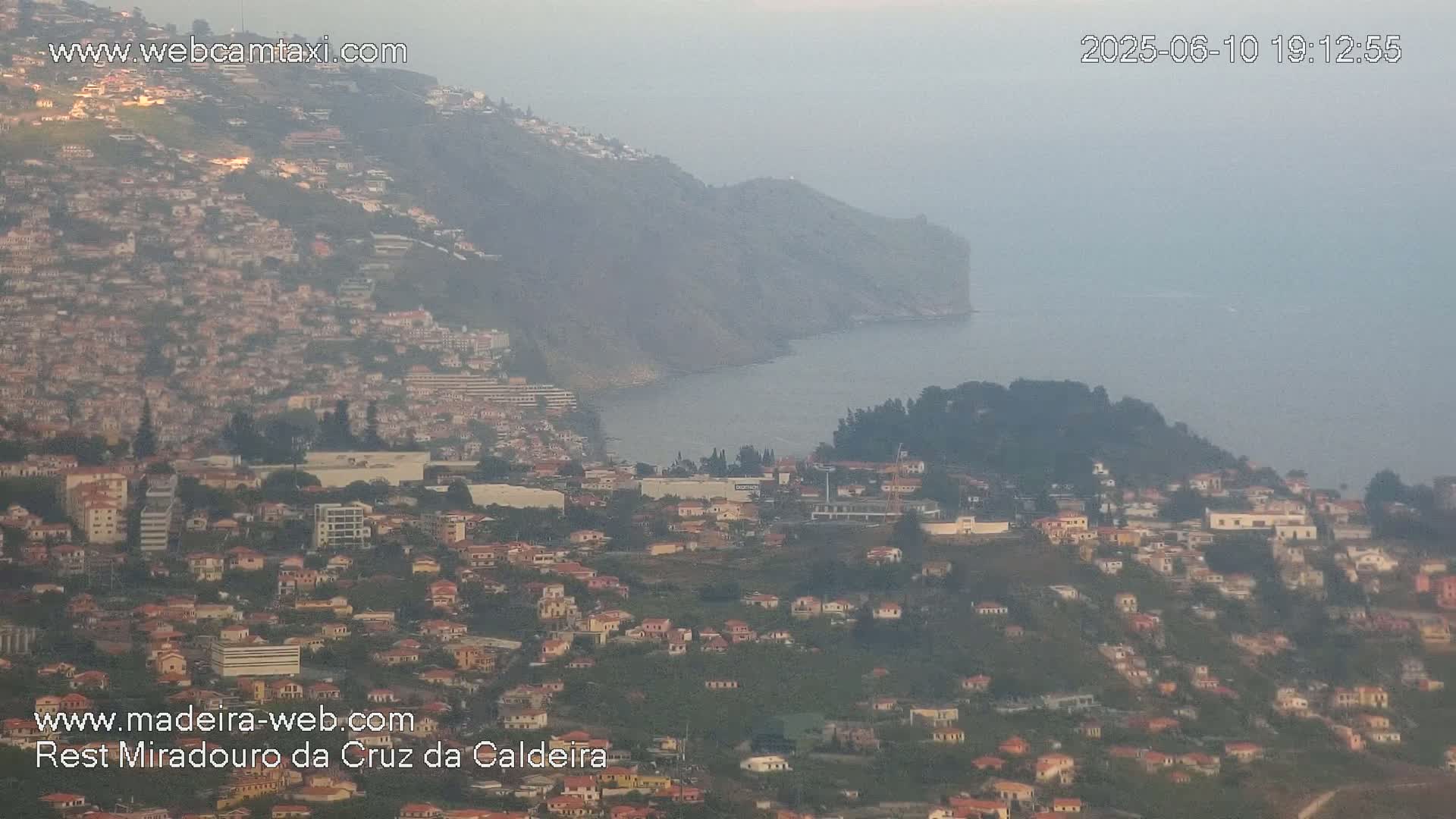 A hazy view shows a coastal town built on a hillside sloping down to the ocean.