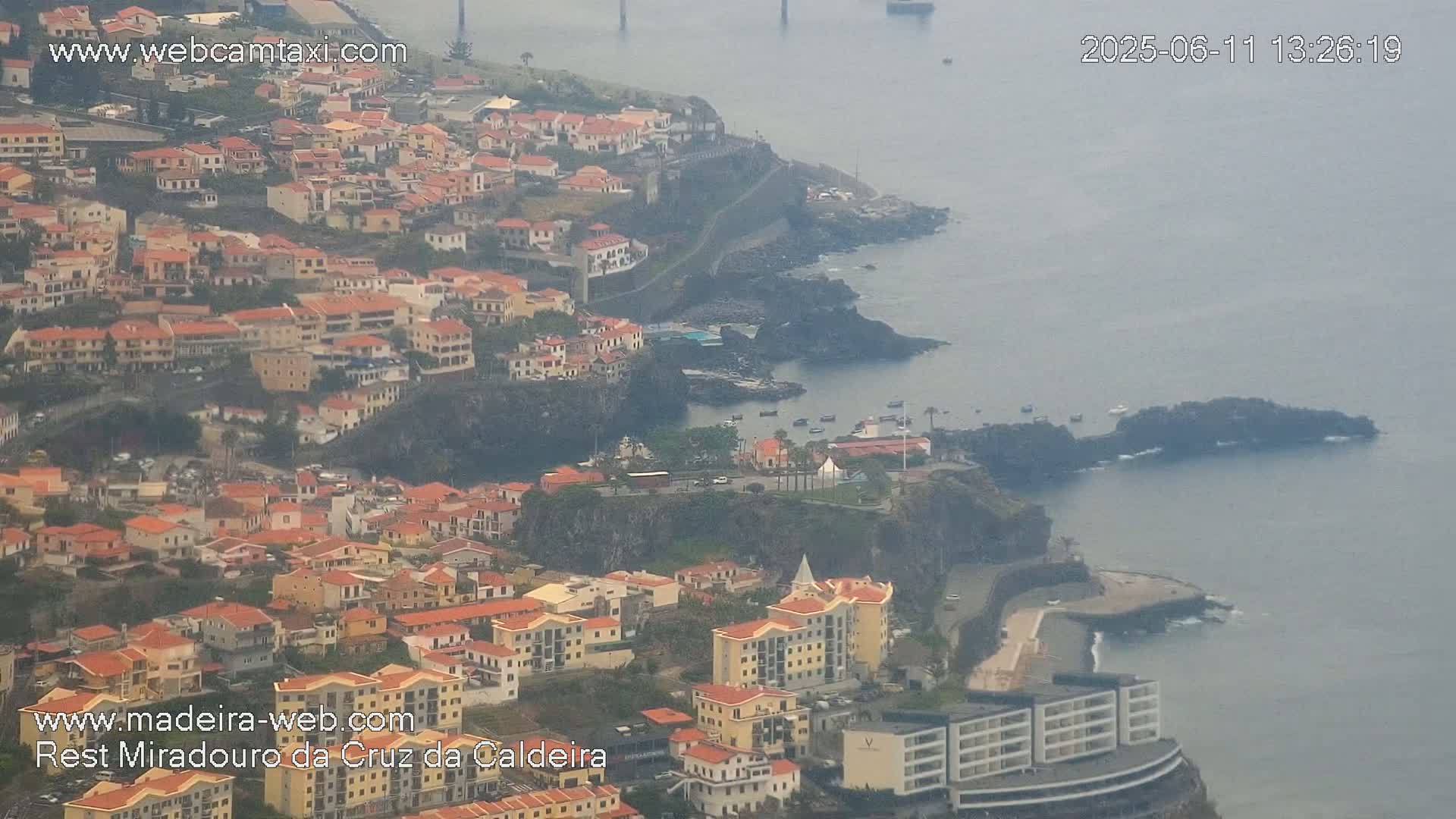 A coastal town with numerous low-rise buildings clings to a cliffside overlooking a hazy ocean.