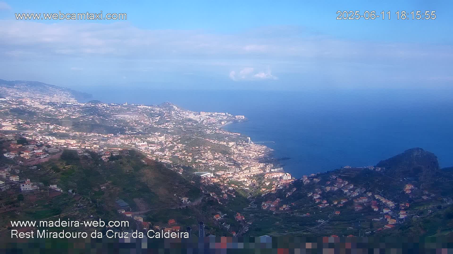 A coastal town nestled on a hillside overlooking a calm ocean under a mostly clear sky.
