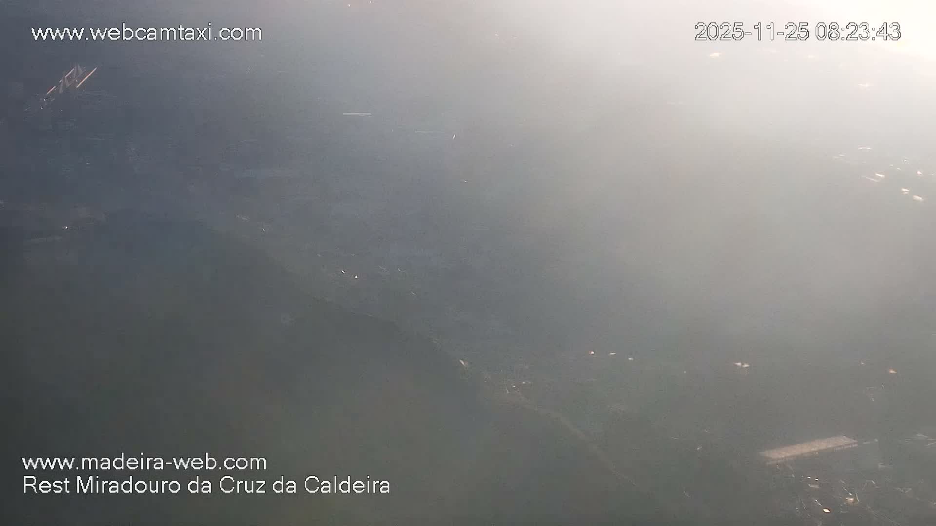 The image depicts an outdoor landscape heavily obscured by dense fog or haze, revealing only faint, scattered distant lights and indistinct terrain due to extremely low visibility.