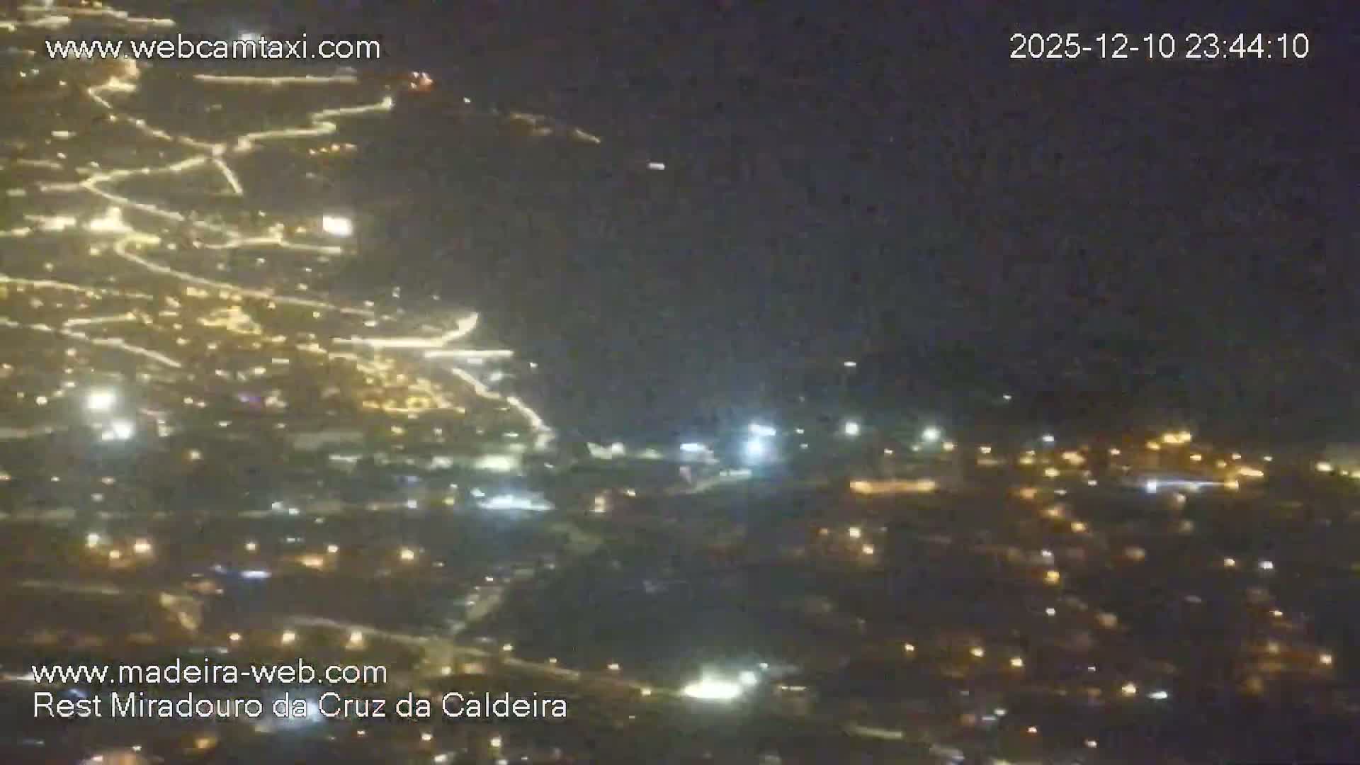 A panoramic nighttime view reveals a sprawling illuminated cityscape with numerous lights tracing roads and structures under a clear, dark sky.