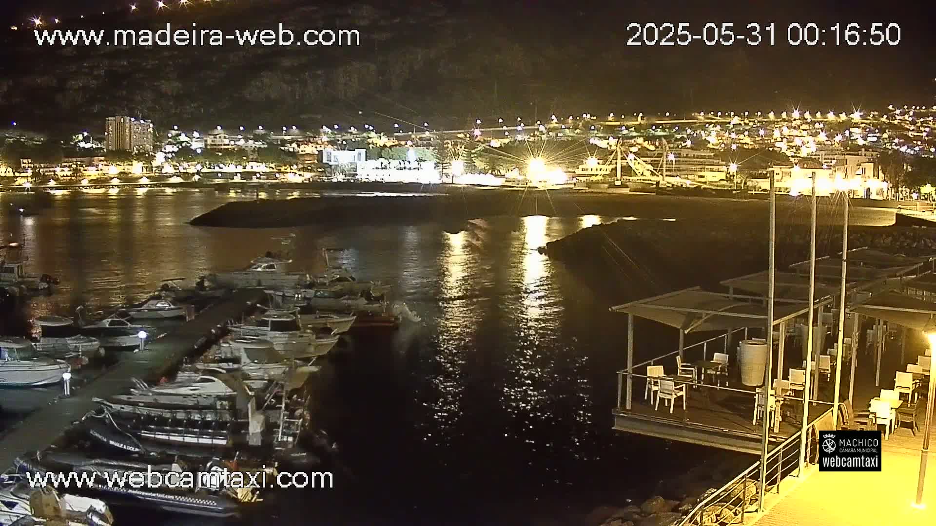 A nighttime view of a harbor filled with boats, adjacent to a waterfront lit with lights, under a clear sky.