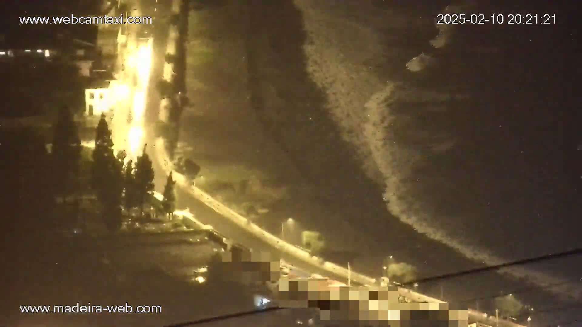 A nighttime, high-angle view shows a brightly lit roadway curving alongside a dark body of water under a cloudy sky.