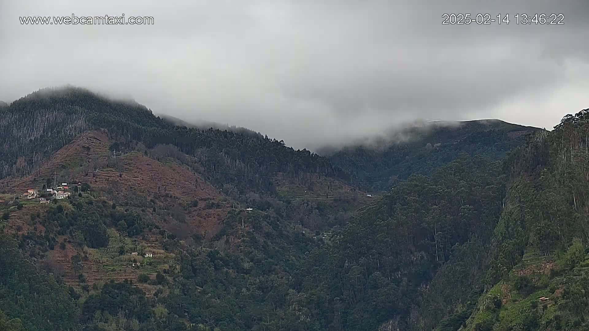 A misty, overcast day reveals a landscape of rolling, forested hills with a small village nestled into one of the hillsides.