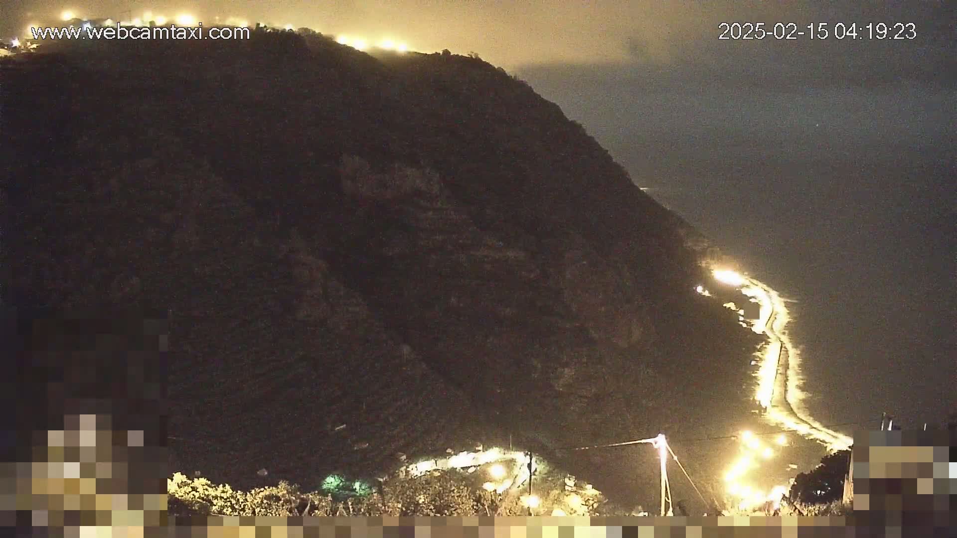 A nighttime view of a dark, mountainous coastline with a winding road illuminated by lights.