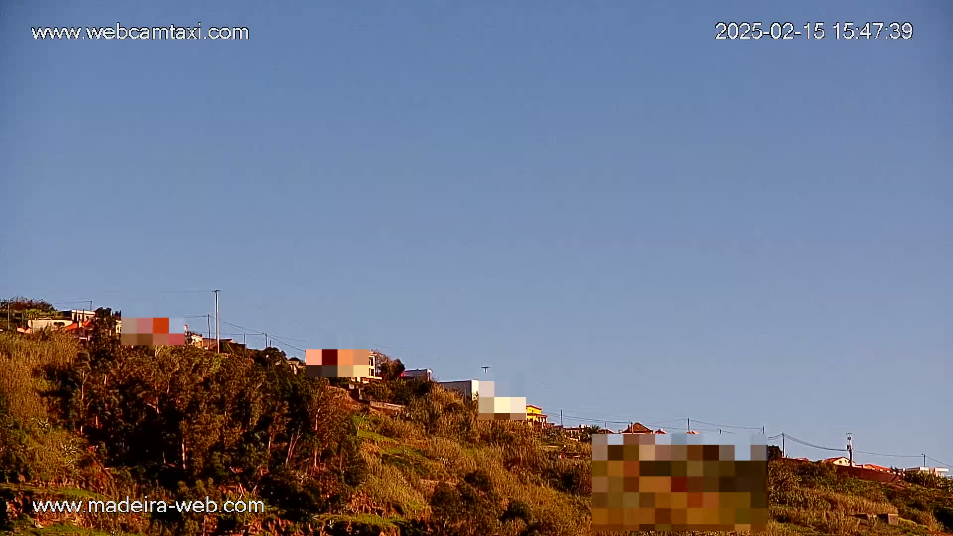 A hillside covered in scrubby vegetation and dotted with houses is visible under a clear blue sky.