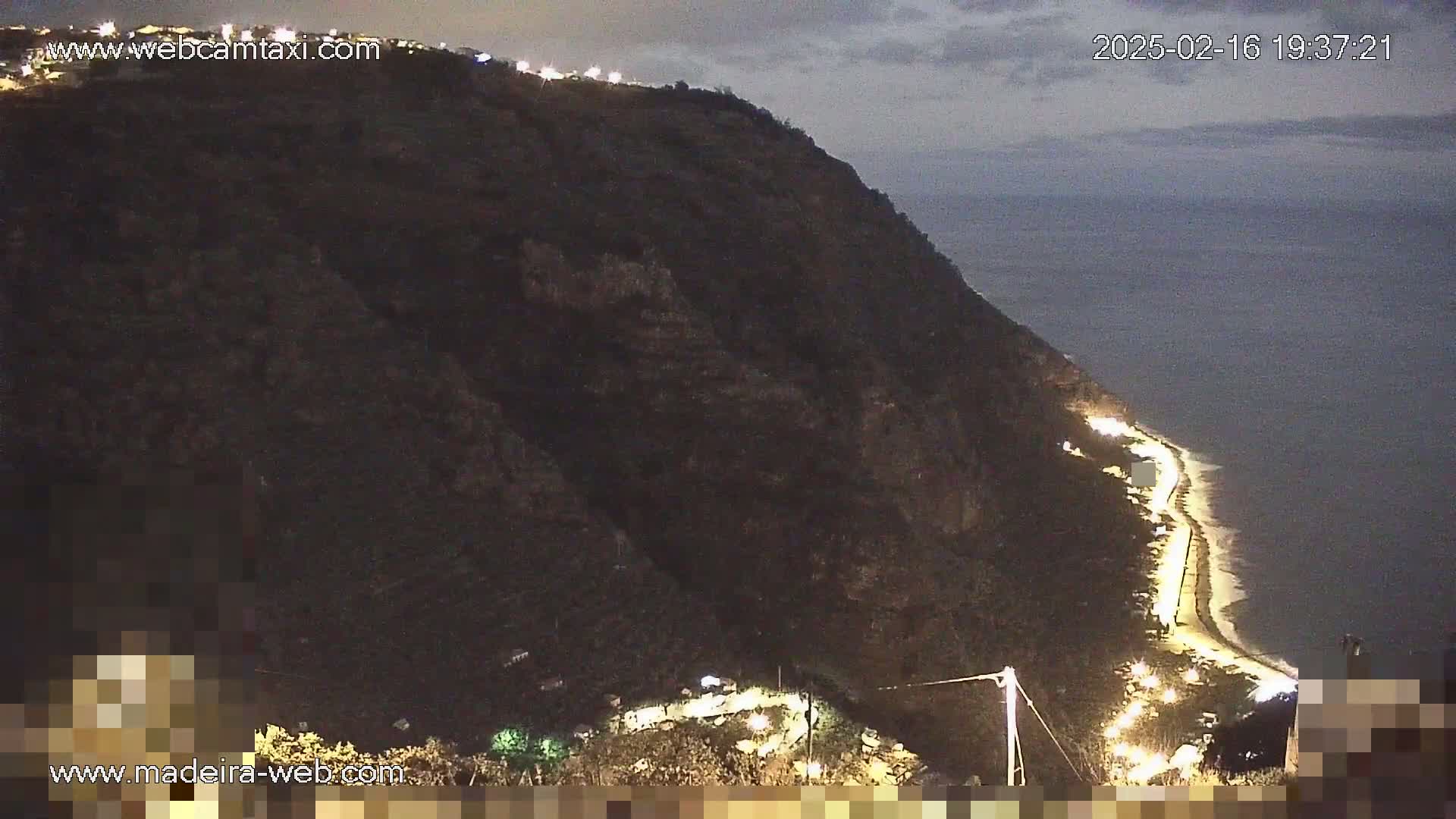 A dark, cliffside overlooks a dimly lit coastal road at night.