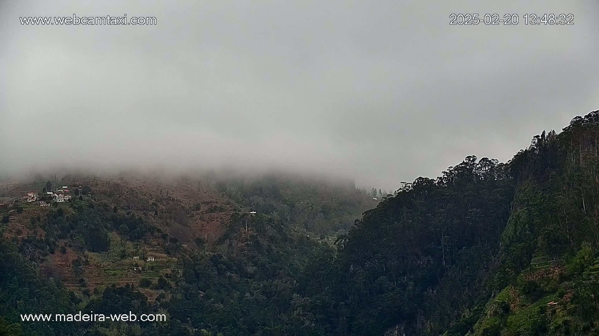 A foggy, mountainous landscape shows dark green vegetation on steep slopes, with a small village nestled in the lower hills.