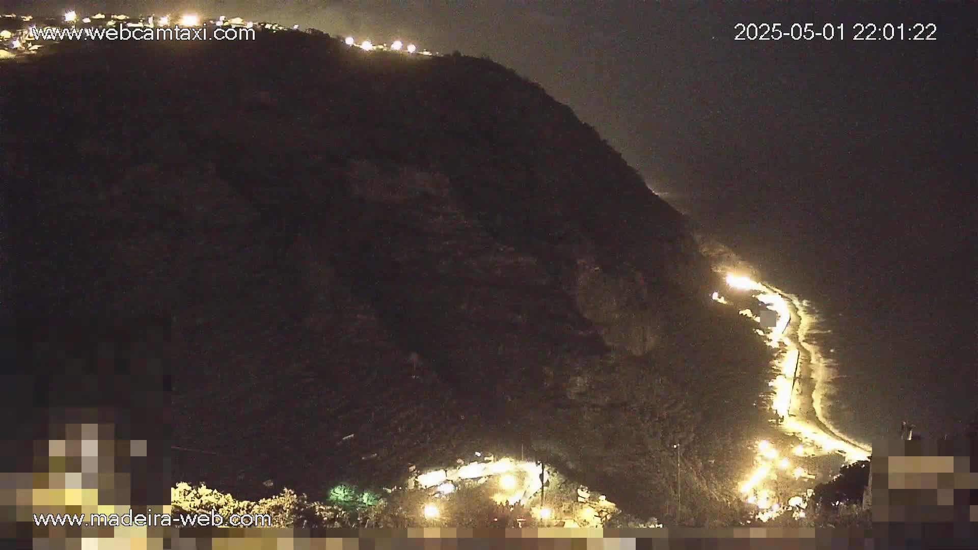 A nighttime view of a dark mountainside with a winding road illuminated by lights below.