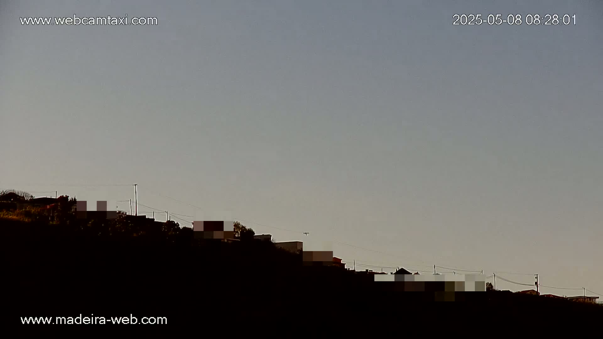 A line of houses sits atop a dark hill under a clear, light gray sky.