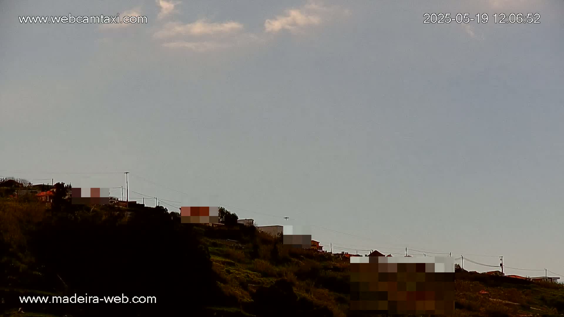 A hillside with houses and sparse vegetation under a mostly clear, pale sky.