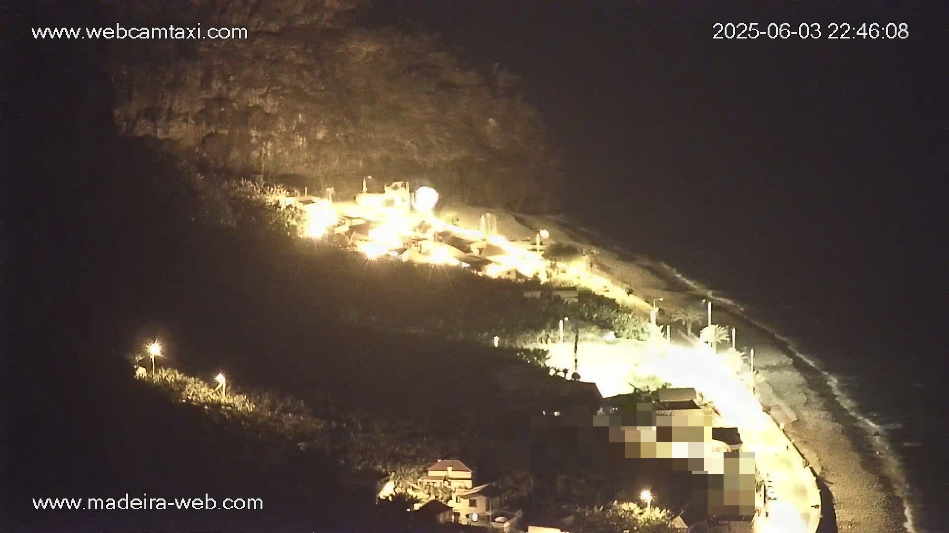 A nighttime aerial view shows a coastline with buildings illuminated along a sandy beach under a dark sky.