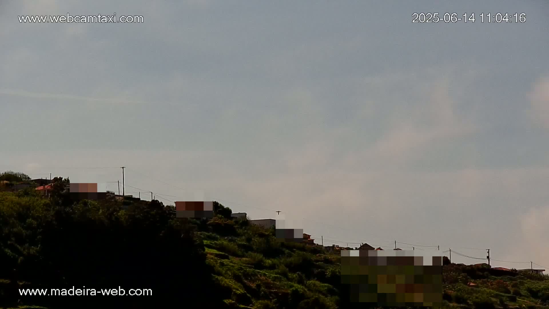 A hillside covered in green vegetation displays a few houses under a mostly cloudy sky.