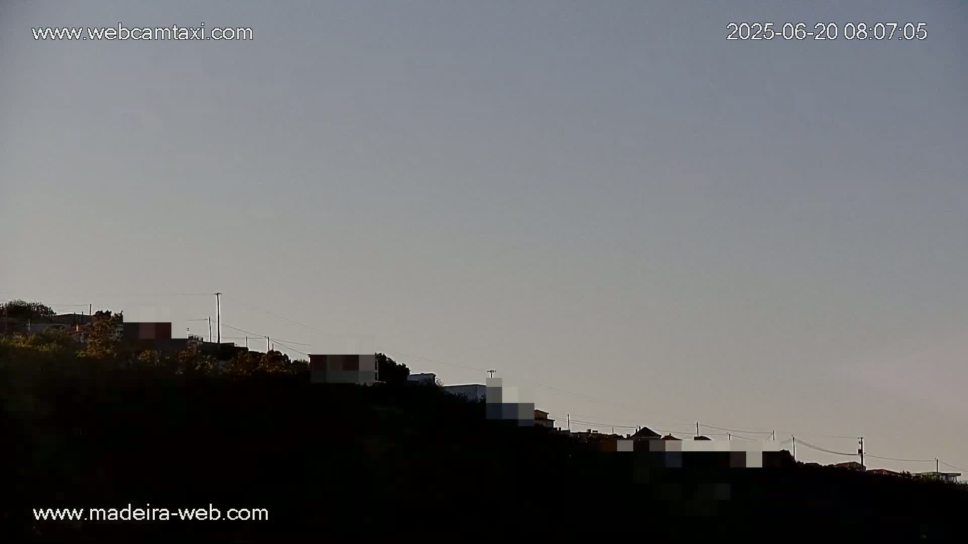 Under a clear, light-grey sky, a hillside dotted with houses is silhouetted against the brightening horizon.