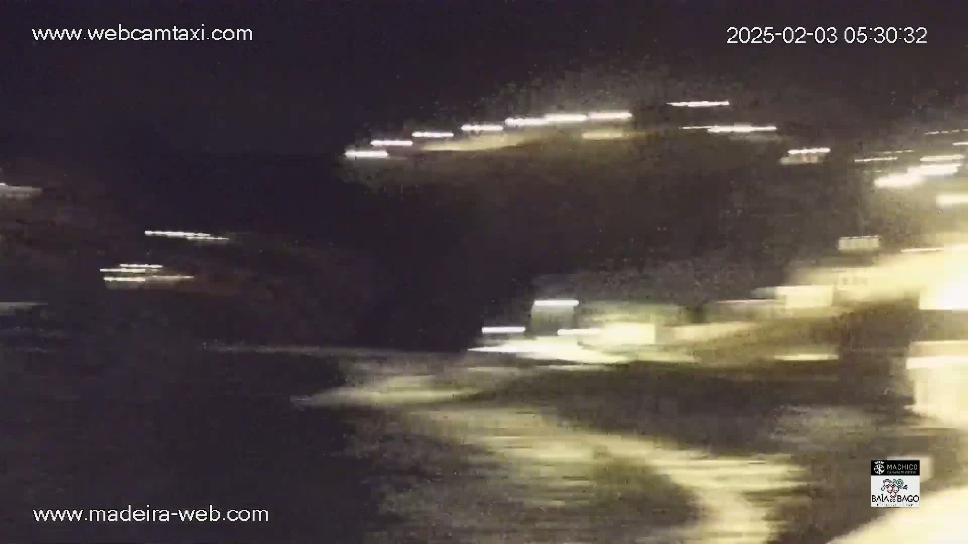 A nighttime, blurry image shows streaks of light from vehicles and buildings near a body of water.