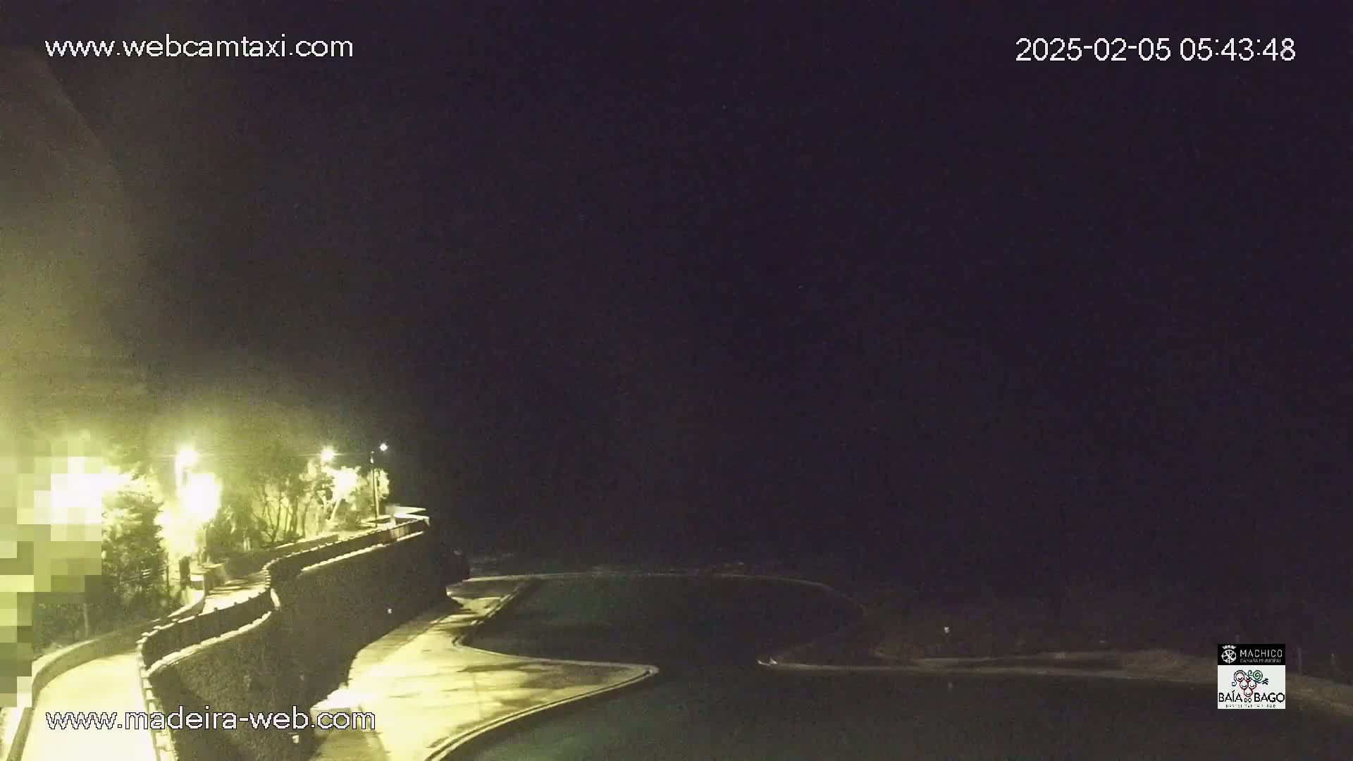 A nighttime view of a curved walkway and swimming pools next to a dark ocean under a clear, dark sky.