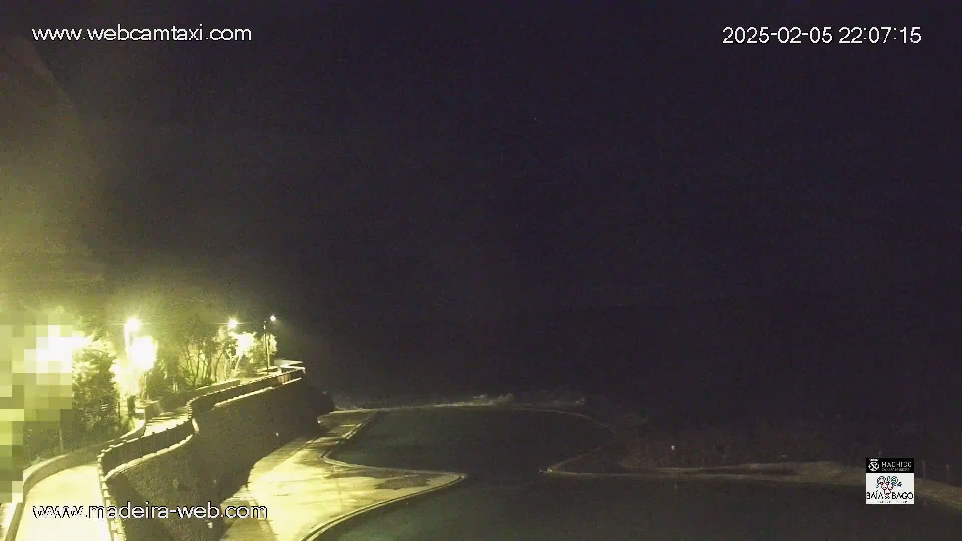A nighttime view of a dark ocean, a curving walkway with lights, and a partially visible pool.