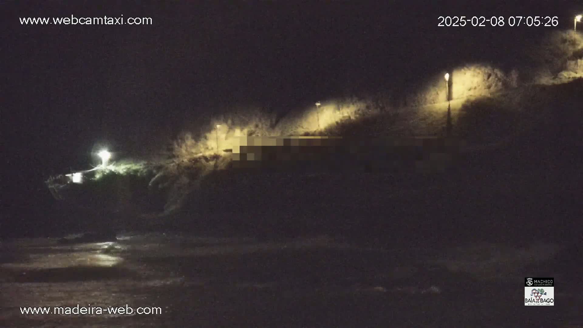 A nighttime, dimly lit coastal scene shows a dark hillside with several illuminated lampposts and a body of water at the bottom.