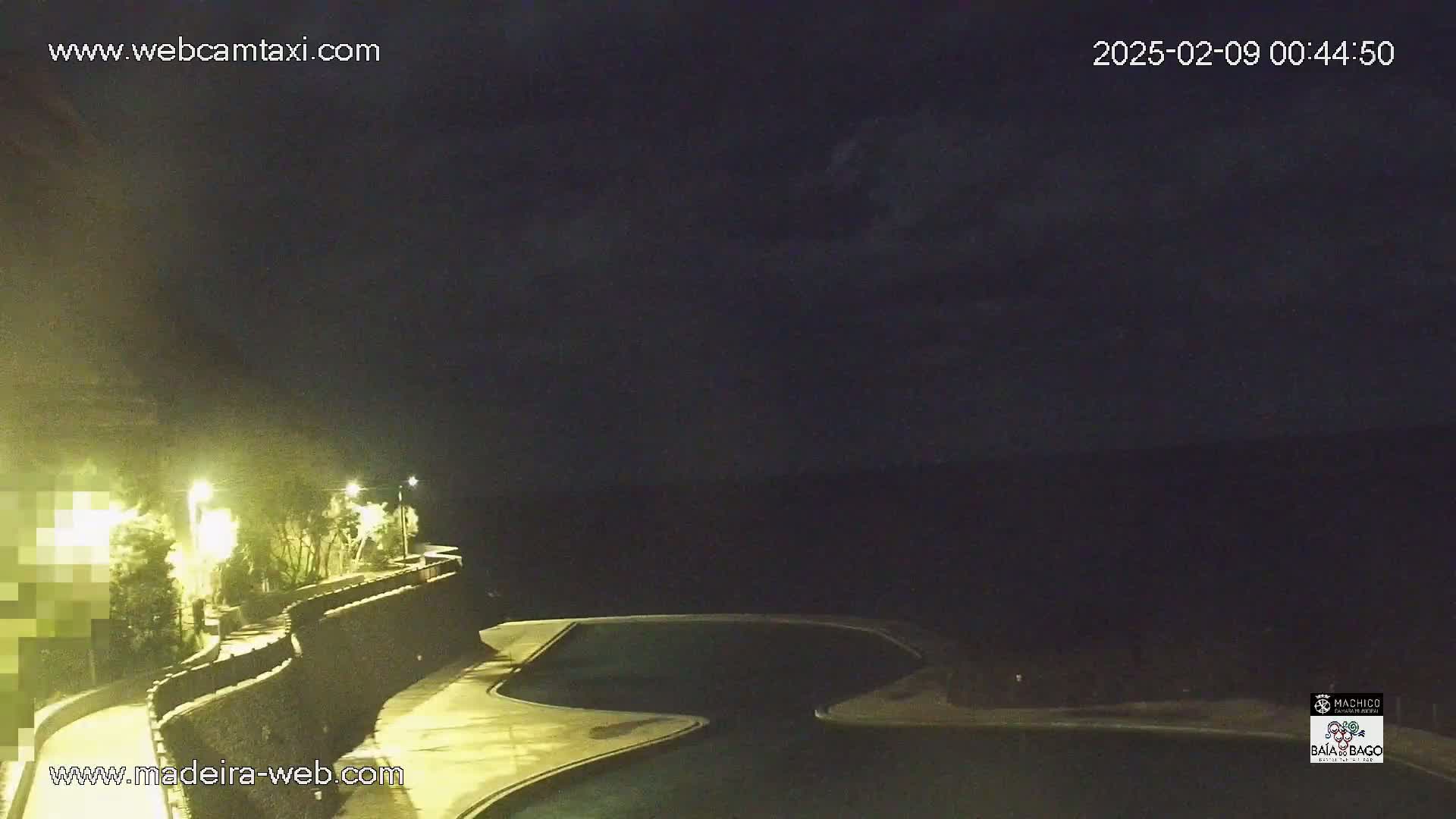 A nighttime view of a dark, mostly cloudy sky over a curved wall surrounding illuminated pools and a walkway.