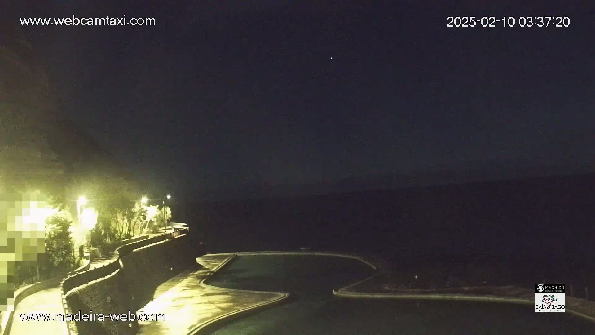 A nighttime view of an outdoor pool area with a curving wall and lights, under a clear, dark sky.