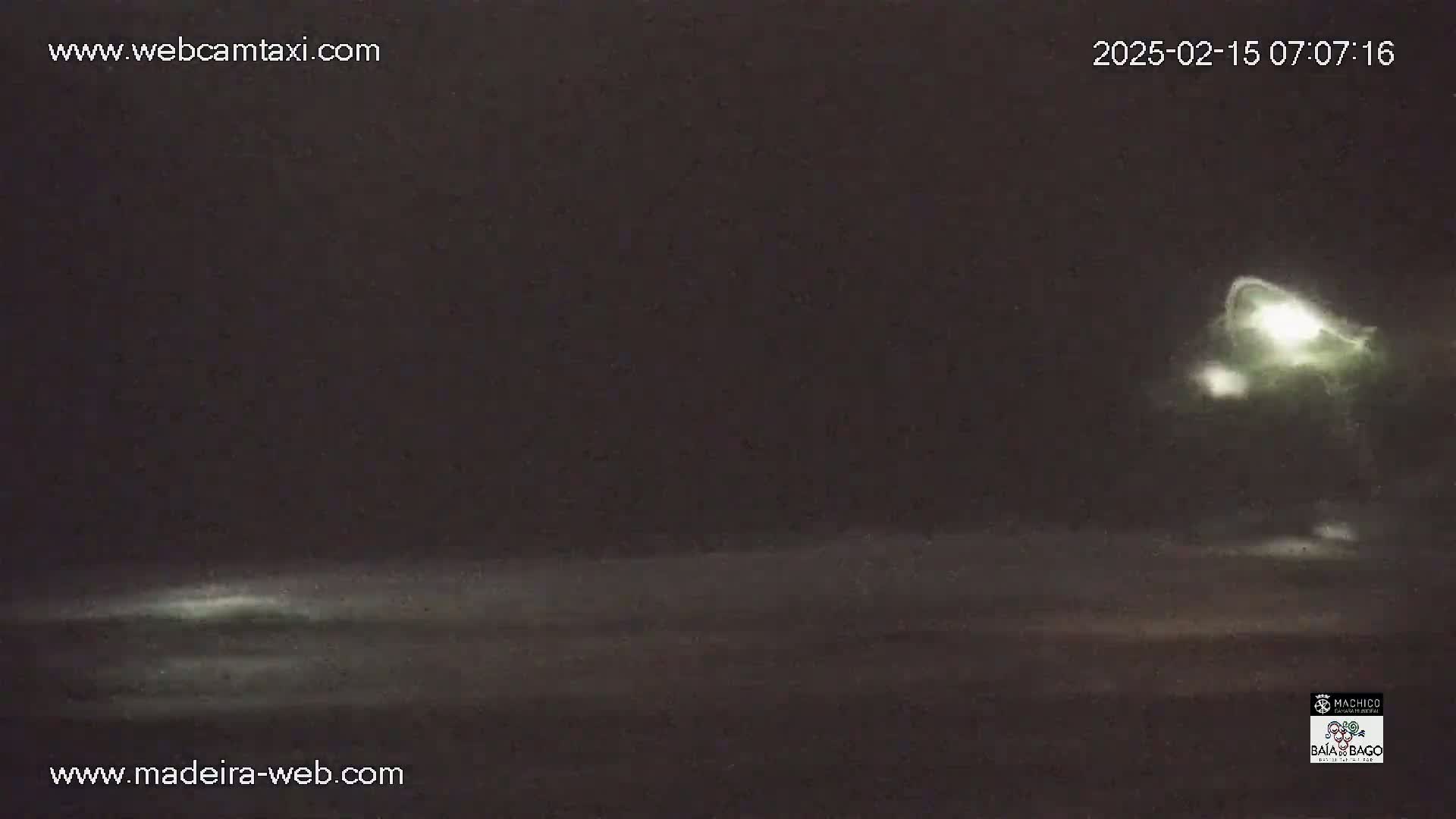 A nighttime, low-light view of a dark body of water with a faint, bright light source visible in the distance.