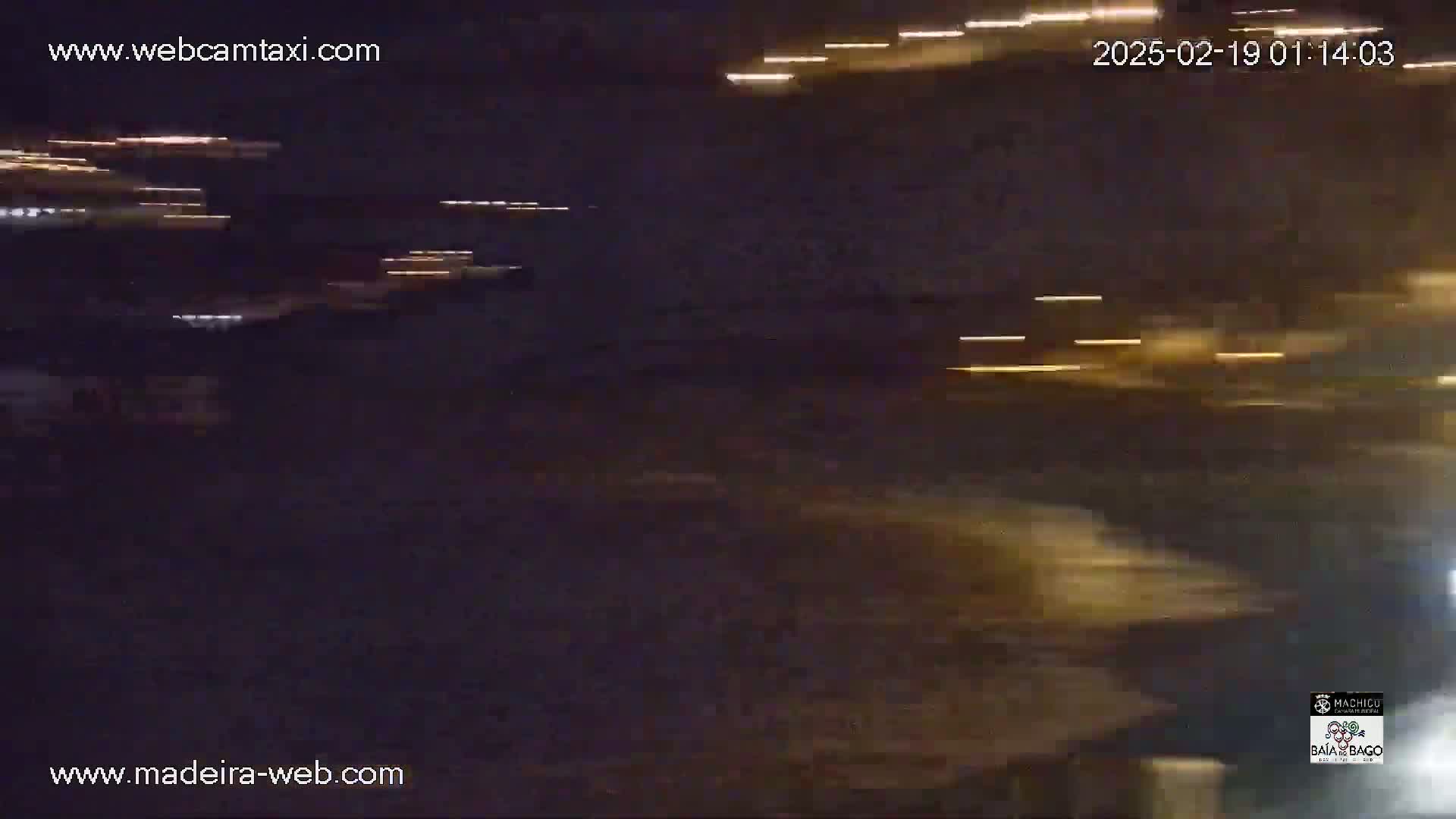 A nighttime, blurry view shows streaks of light from moving vehicles, possibly on a road near a body of water.