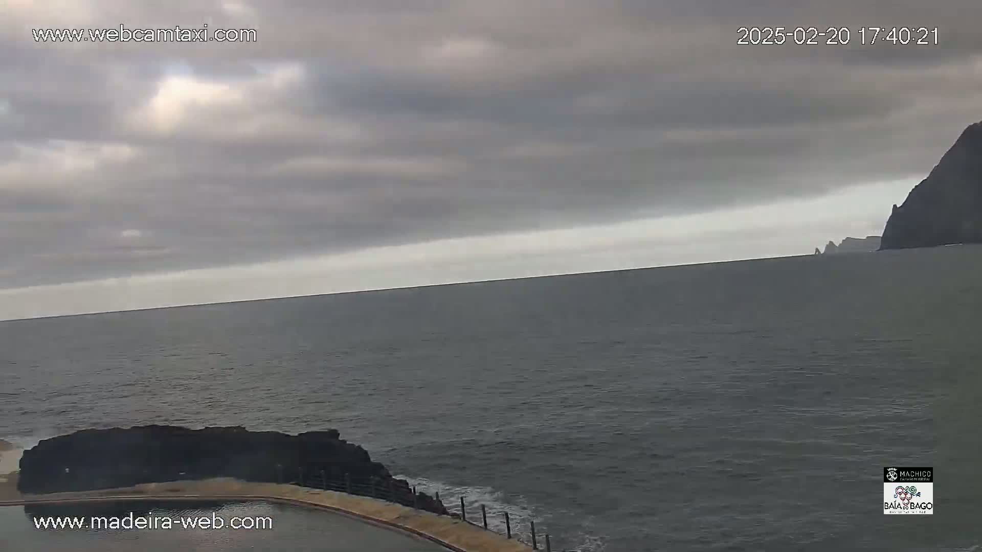 A calm, gray ocean stretches to a distant, dark coastline under a cloudy sky.