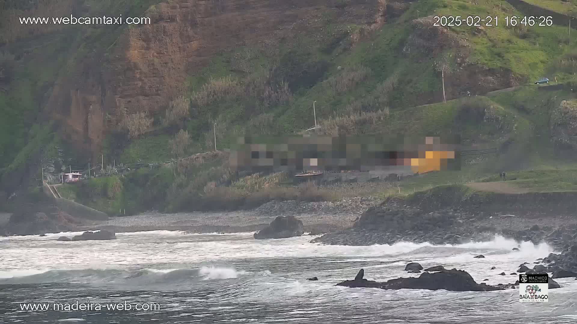 A rocky coastline with a small beach is met by a gray, choppy ocean under an overcast sky.