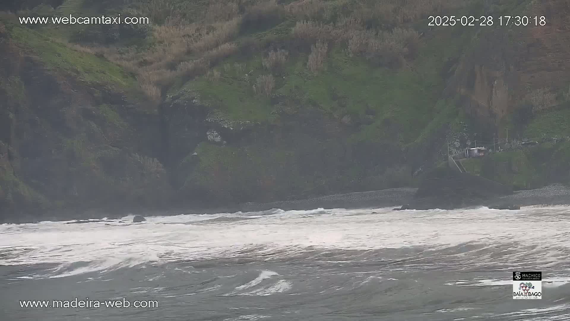 A rocky, green hillside overlooks a choppy, gray ocean with whitecaps under an overcast sky.