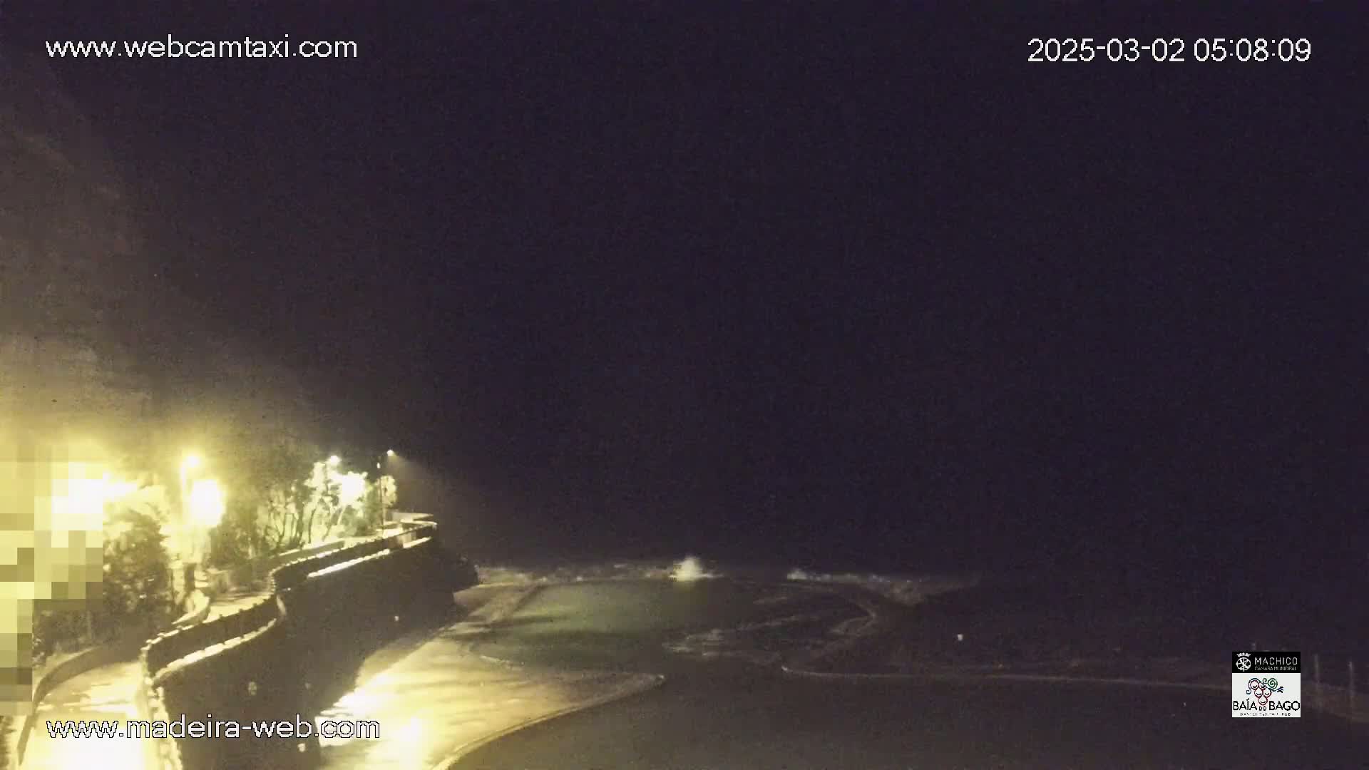 A nighttime view of a rocky coastline with waves crashing near a pool of water, under a dark sky.