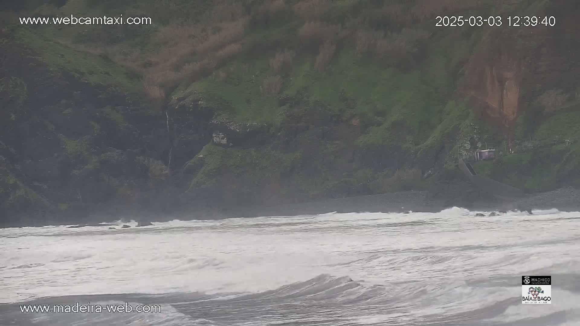 A rocky, green hillside overlooks a turbulent, gray ocean with choppy waves.
