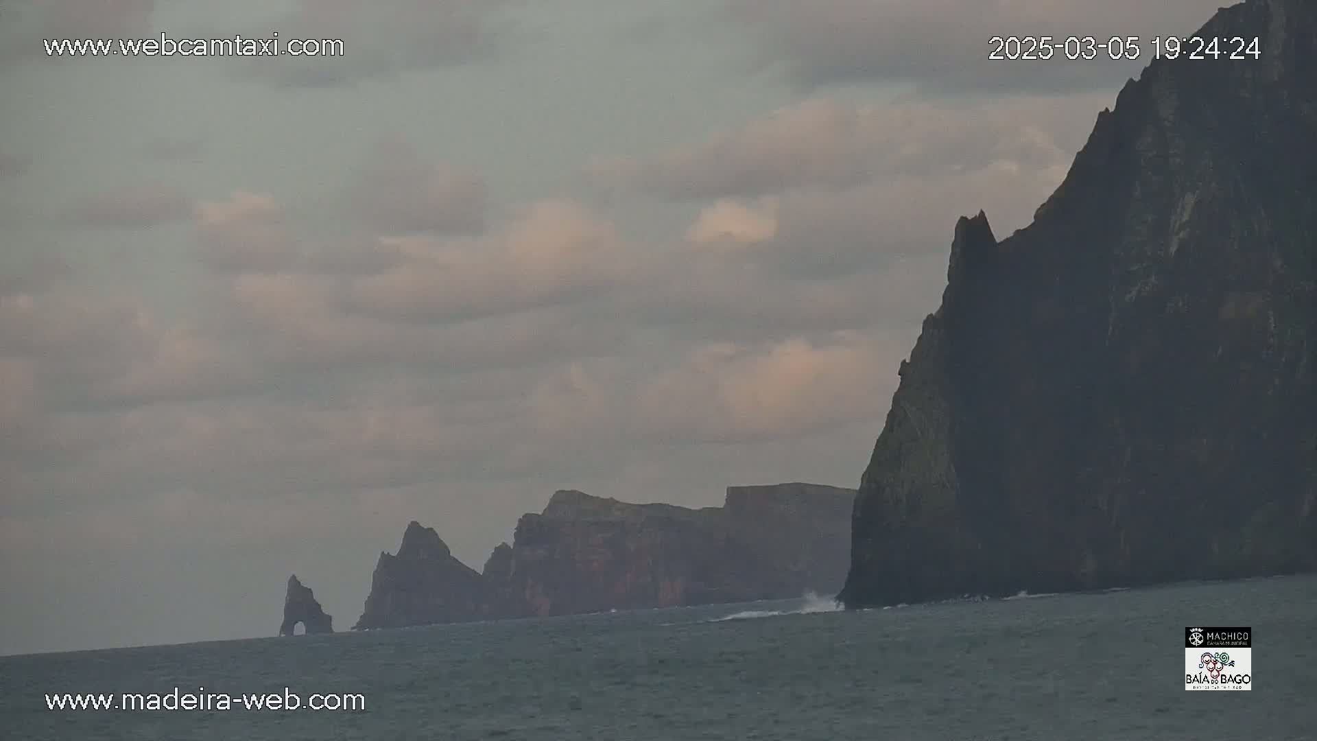 Dark, rocky cliffs rise from a gray ocean under a cloudy sky.